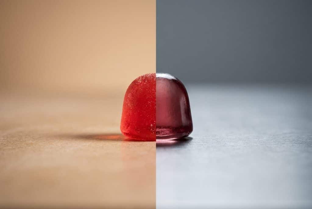 A single red functional gumdrop sits perfectly centered on a studio table, illuminated by warm inviting light on its left half and harsh sterile light on its right half.