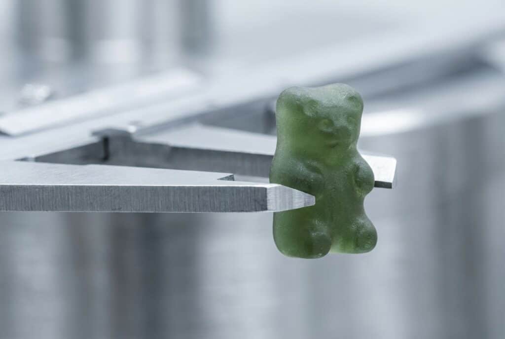 A single botanical green functional gummy being precisely measured by the heavy steel jaws of an industrial micrometer caliper.